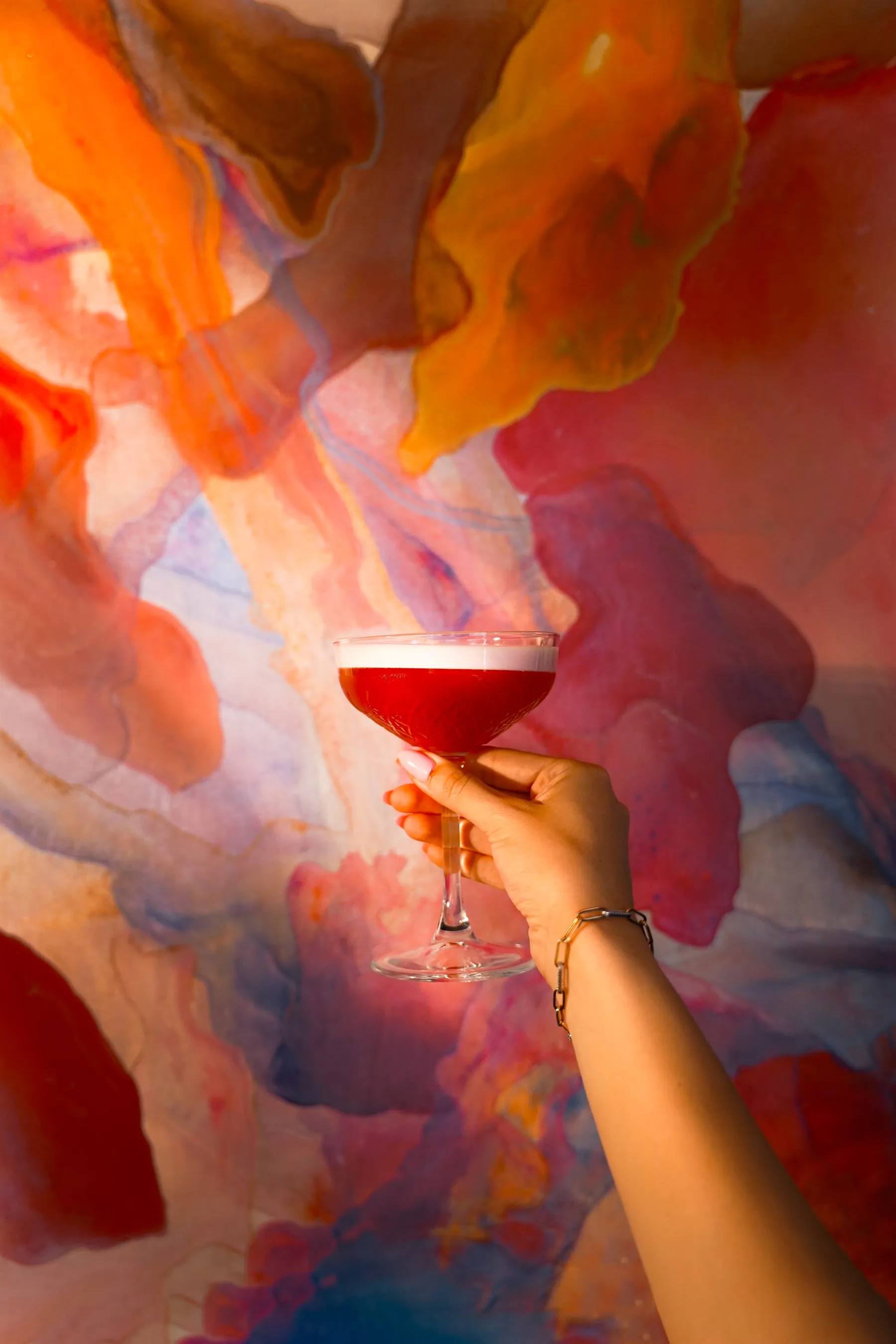 A crimson coupe cocktail raised against a wall of burning sunset colours